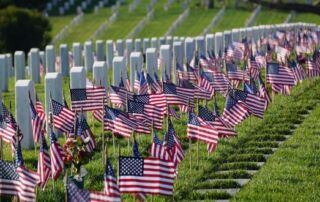 United States Military Cemetery with row of white stone markers with small US flags in the ground in front of each marker.