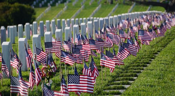 United States Military Cemetery with row of white stone markers with small US flags in the ground in front of each marker.